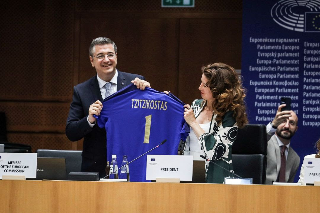 Απόστολος Τζιτζικώστας με μια γυναίκα και κρατάει αθλητική μπλούζα